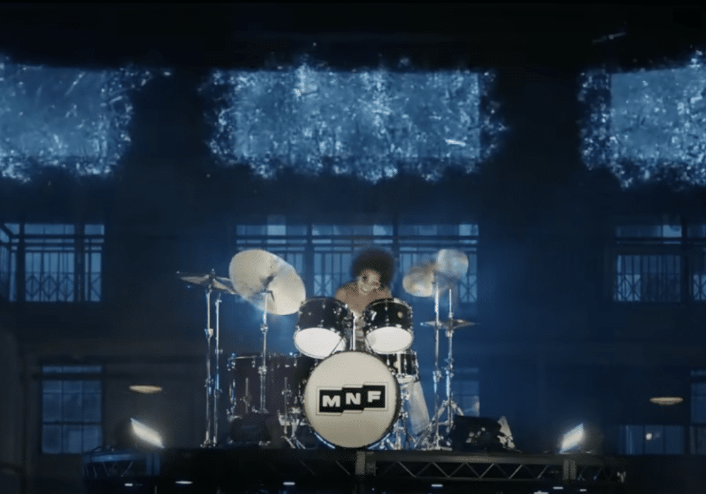 Blackman sits behind a drum set with the letters "MNF" printed on the bass.